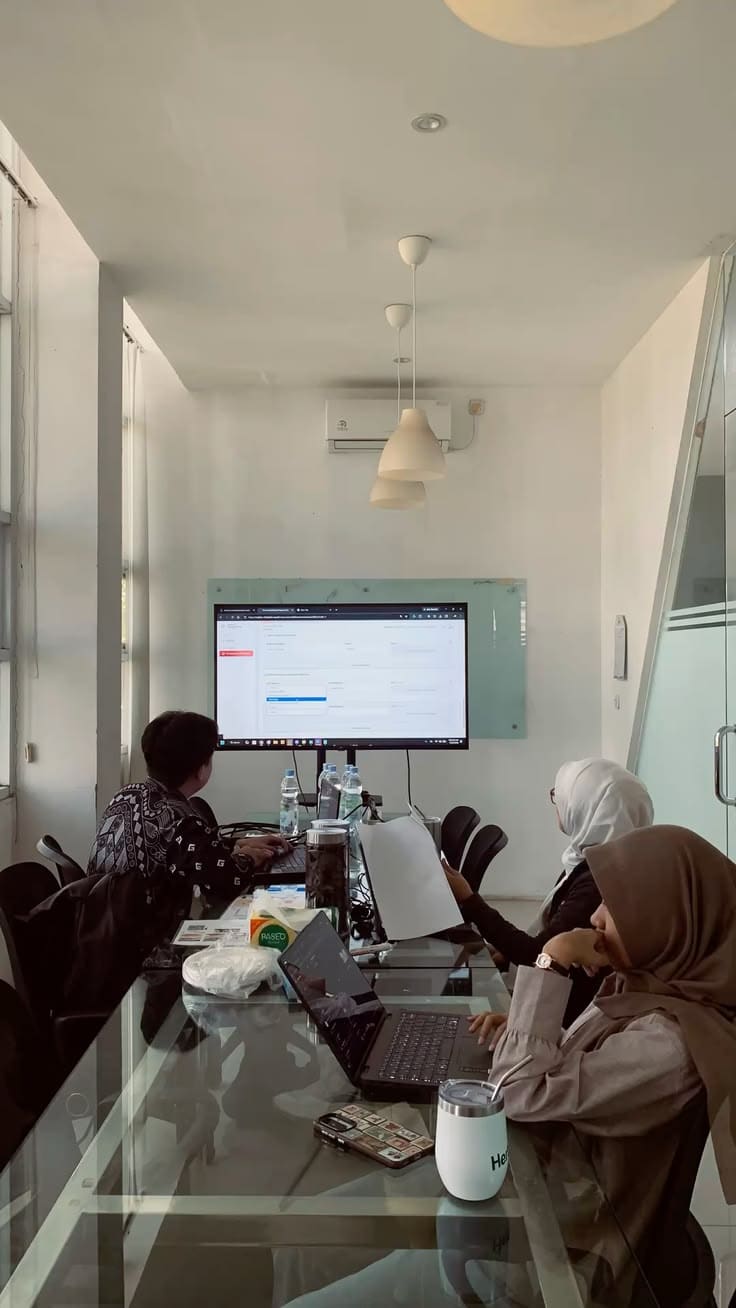 Tim berdiskusi di depan layar dalam ruang rapat